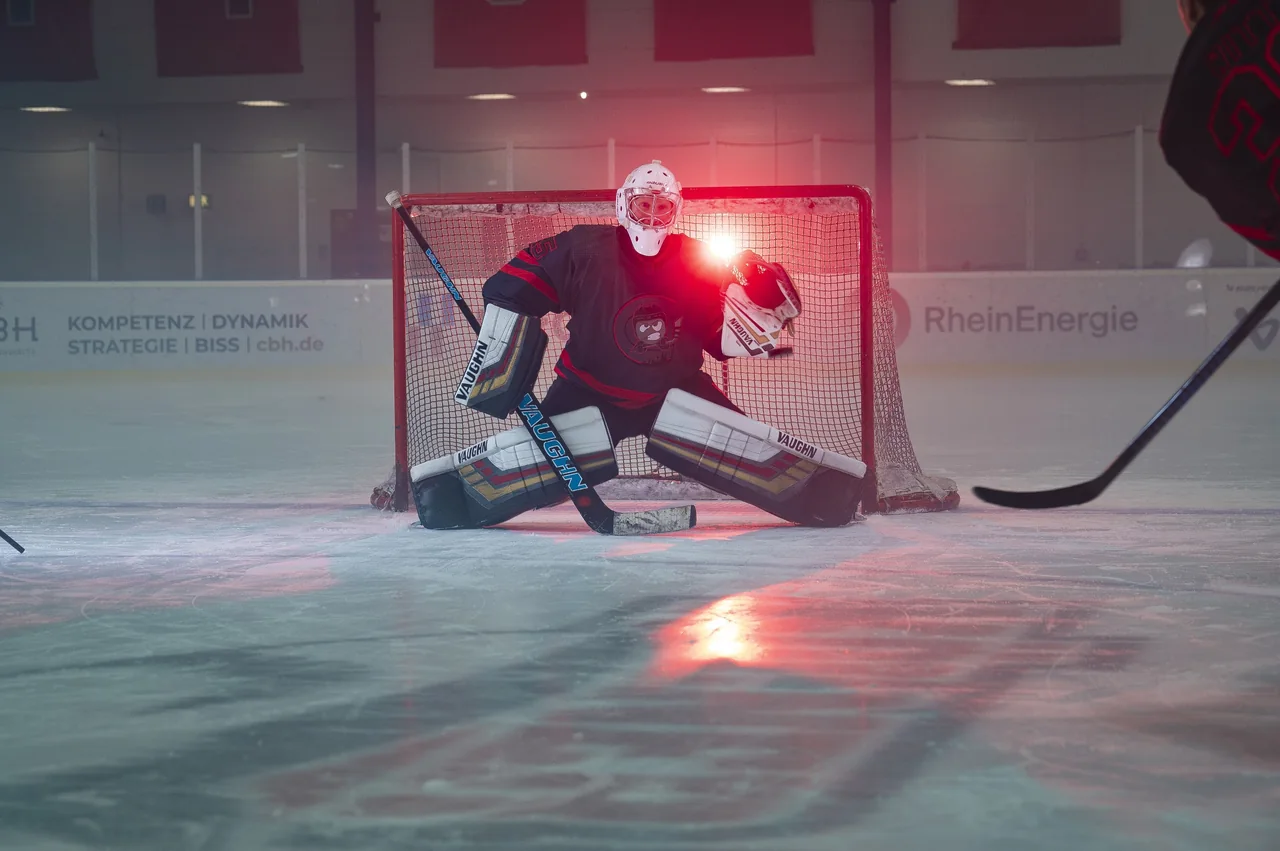 Eishockey-Torwart in Abwehrhaltung vor dem Tor im roten Gegenlicht
