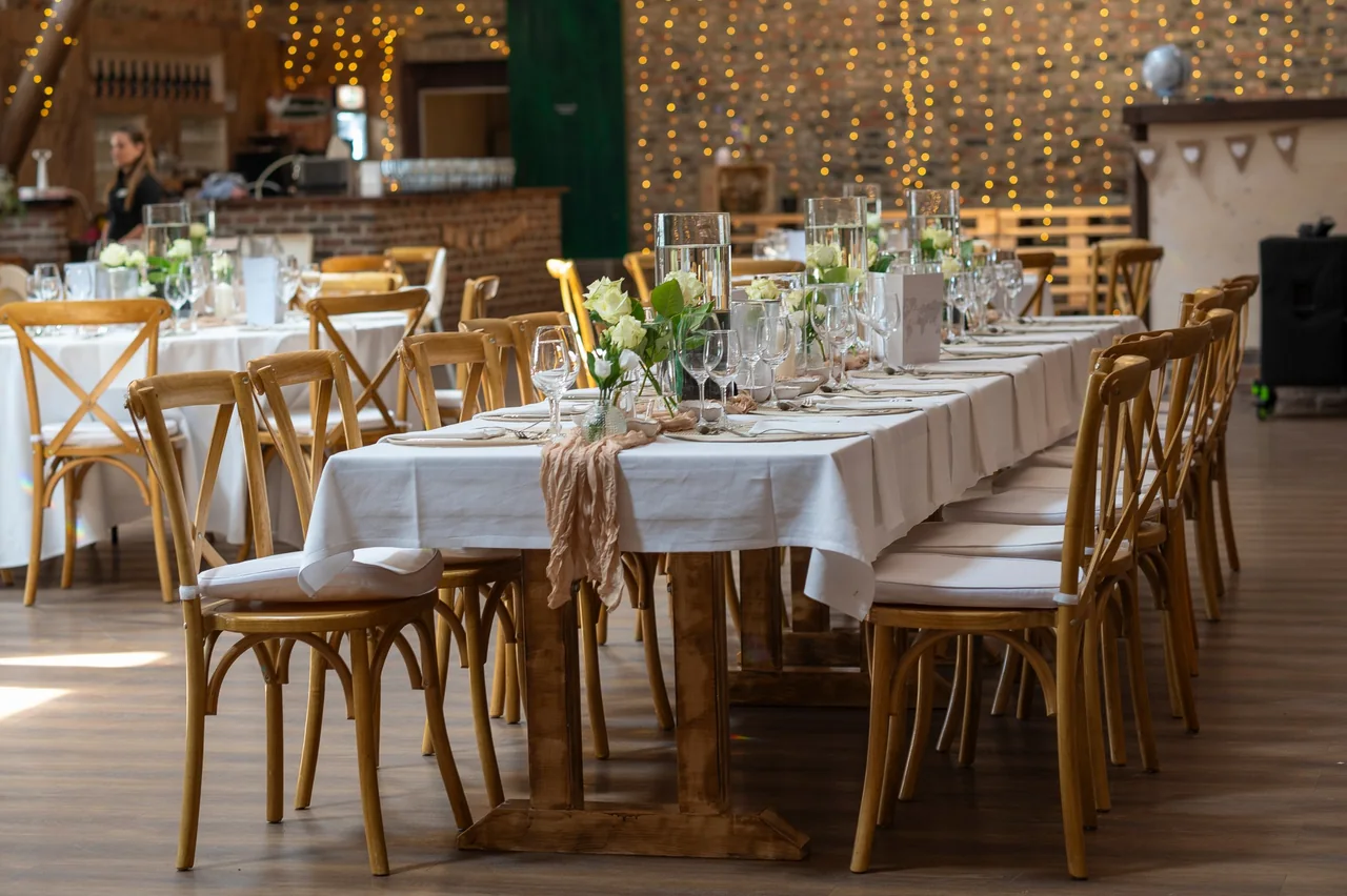 Festlich gedeckte Hochzeitstafel mit weißen Rosen und Lichterketten in einer Scheune