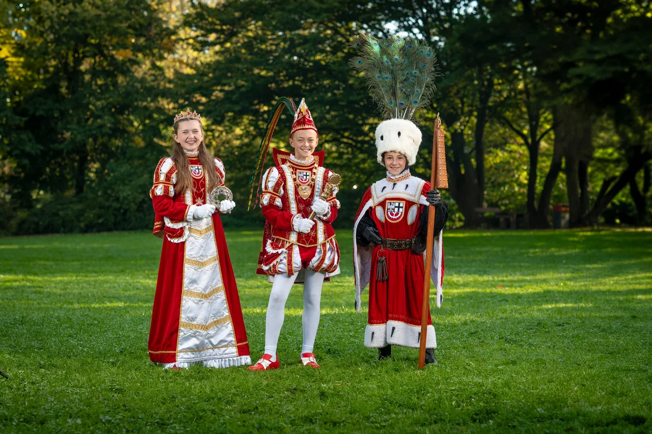 Kinderdreigestirn mit Jungfrau, Prinz und Bauer im Ornat auf einer Wiese im Park