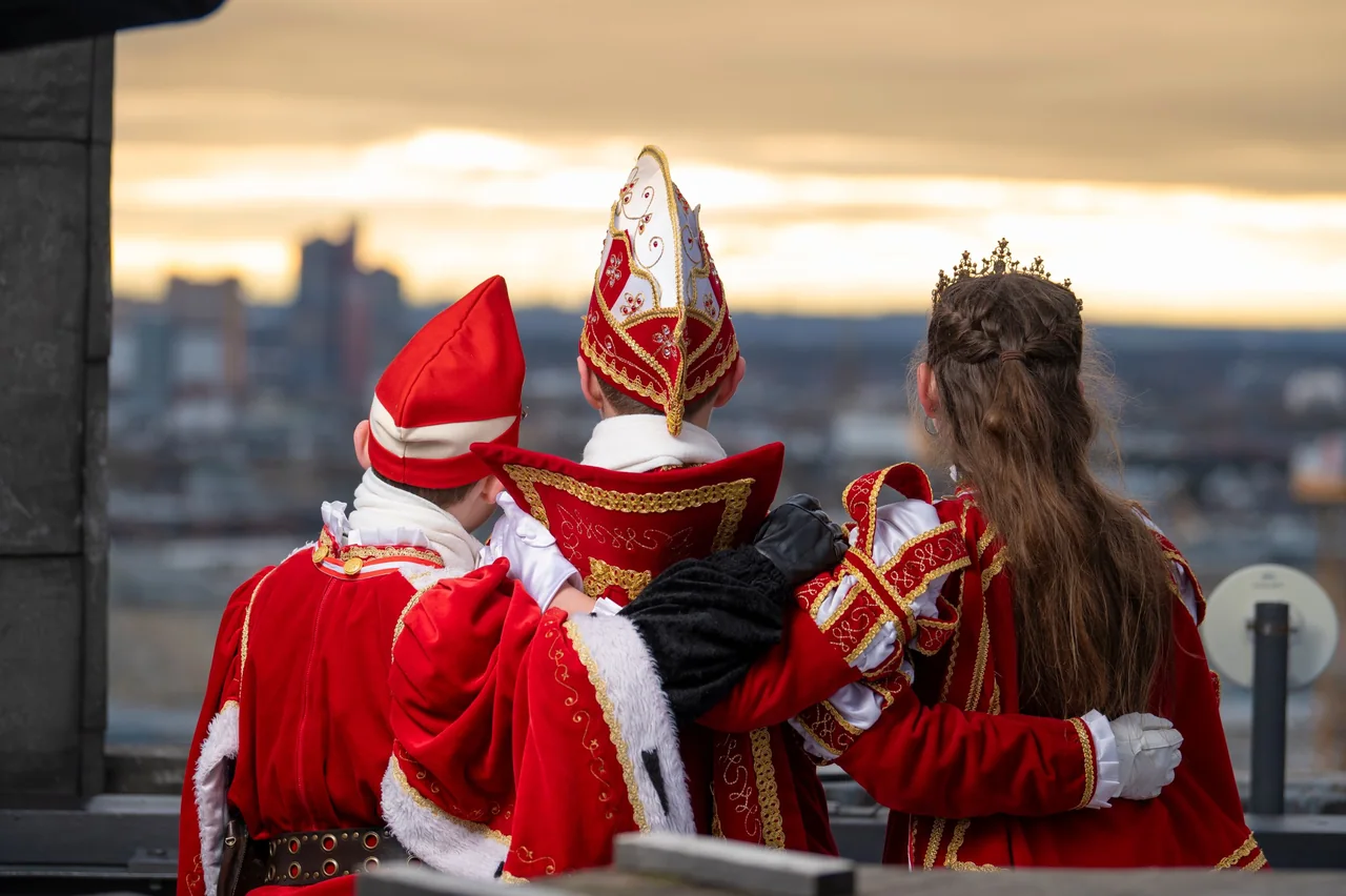 Kinderdreigestirn im Ornat von hinten, Arm in Arm mit Blick über die Stadt im Abendlicht