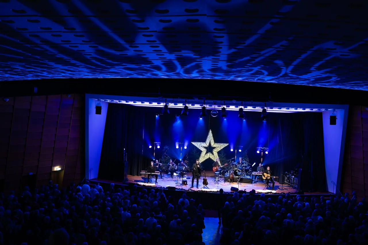 Konzertsaal mit voller Bühne, leuchtendem Stern und blauem Licht über dem Publikum