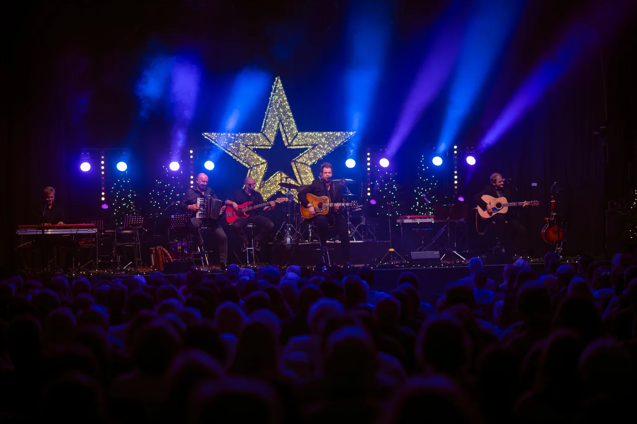 Band auf der Bühne vor einem leuchtenden Stern im blauen Scheinwerferlicht, davor das Publikum